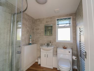 A bathroom with a shower, sink, toilet, window with a fish-patterned blind and tiled walls at Beachcomber in Norton Park near Dartmouth