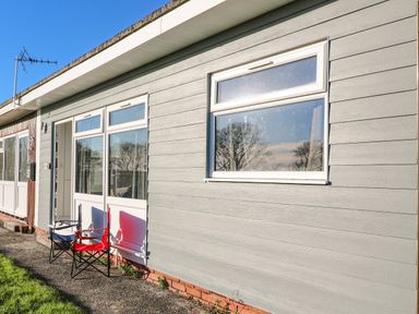 The exterior of a building with grey siding white framed windows and two folding chairs outside Beachcomber Norton Park near Dartmouth