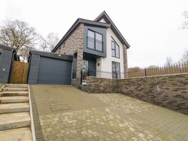 A modern two-story house with a brick and plaster exterior and a closed garage door with driveway and steps at Ty Bains in Llanberis