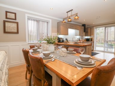 A dining area with a wooden table set with bowls plates glasses and cutlery with leather chairs and a kitchen in the background at Ty Bains in Llanberis