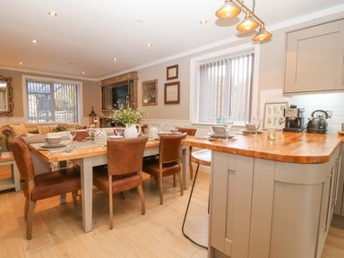 A dining area with a wooden table and brown chairs next to a kitchen counter with stools and appliances at Ty Bains in Llanberis