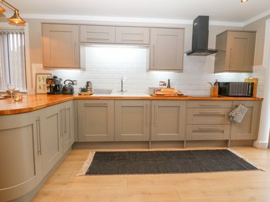 A kitchen with wooden countertops grey cabinets a black rug and appliances at Ty Bains in Llanberis