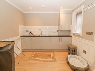 A utility room with cabinets a sink a drying rack a laundry basket and a pet bed at Ty Bains in Llanberis