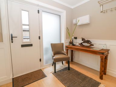 An entryway with a white door a brown chair and a wooden table with a plant and a rocking horse at Ty Bains in Llanberis