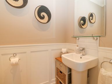 A small bathroom with a pedestal sink a cabinet with wicker drawers a towel ring with a towel and wall decorations at Ty Bains in Llanberis