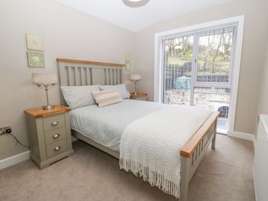 A bedroom with a bed a bedside table with lamps and a window with vertical blinds at Ty Bains in Llanberis