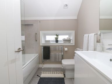 A bathroom with a bathtub a toilet a sink a towel rack with towels a small window and a plant at Ty Bains in Llanberis