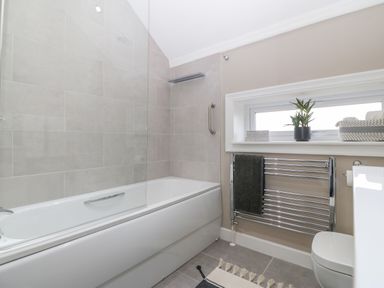 A bathroom with a bathtub, towel rack, small window with plant, and toilet at Ty Bains in Llanberis