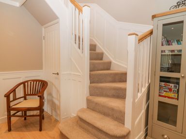 A carpeted staircase with white banisters next to a wooden chair and a cabinet with glass doors at Ty Bains in Llanberis