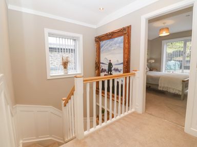 A stairway landing with a large framed painting and a window with vertical blinds next to a bedroom at Ty Bains in Llanberis