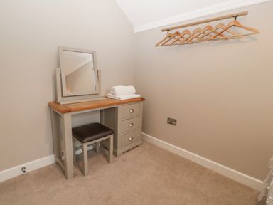 A dressing table with a mirror and stool and wooden hangers on a wall at Ty Bains in Llanberis