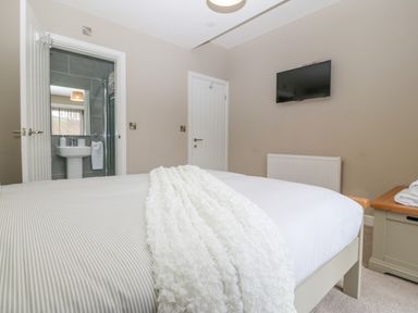 A bedroom with a bed with white linens a wall-mounted television a door leading to a bathroom and a wooden chest at Ty Bains Llanberis