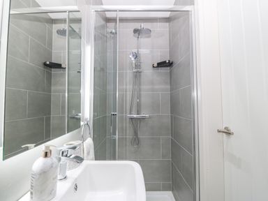 A bathroom with a shower enclosure tiled in gray and a white sink with soap dispenser at Ty Bains in Llanberis