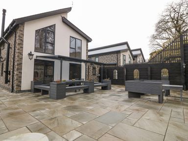 An outdoor patio area with modern benches tables and planters next to a two story house at Ty Bains in Llanberis
