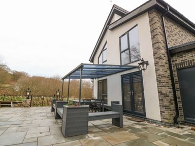 An outdoor patio with built in benches and a table under a glass canopy at Ty Bains in Llanberis