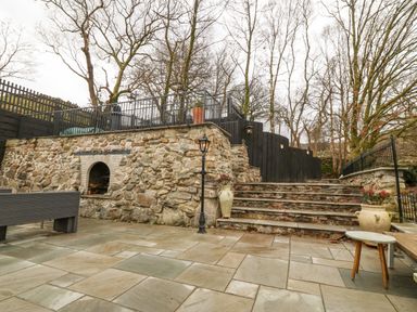 An outdoor stone patio area with stairs leading up to a fenced terrace and bare trees at Ty Bains in Llanberis