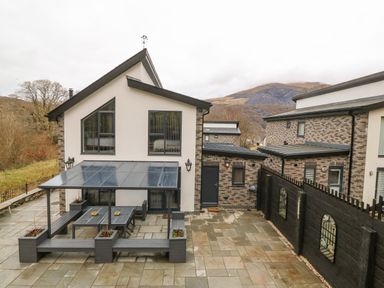 An outdoor patio with a covered seating area and a table beside a modern house at Ty Bains in Llanberis