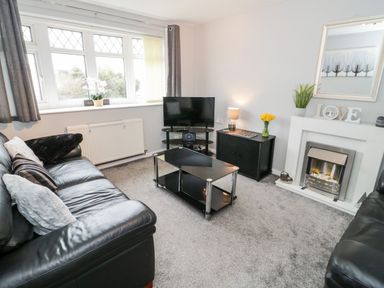 A living room with black leather sofas a glass coffee table a television on a stand and a fireplace at 17 Ffordd Gwenllian in Llanfairpwllgwyngyll