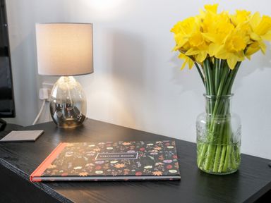 A table with a lamp visitors book and a glass vase with yellow flowers at 17 Ffordd Gwenllian in Llanfairpwllgwyngyll
