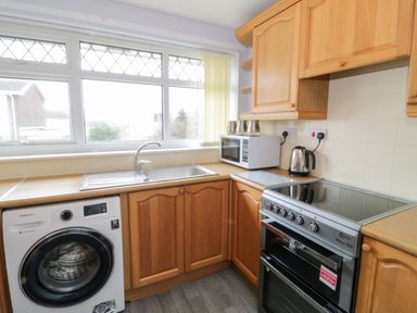 A kitchen with wooden cabinets a washing machine a sink an electric stove a microwave and a kettle at 17 Ffordd Gwenllian in Llanfairpwllgwyngyll