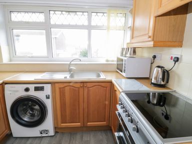 A kitchen with a washing machine sink microwave kettle and stove at 17 Ffordd Gwenllian in Llanfairpwllgwyngyll