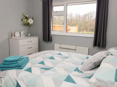A bedroom with a bed covered in geometric patterned bedding and folded towels next to a chest of drawers with flowers and decorative letters at 17 Ffordd Gwenllian in Llanfairpwllgwyngyll