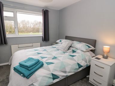 A bedroom with a bed covered with patterned bedding and folded towels beside a nightstand with a lamp at 17 Ffordd Gwenllian in Llanfairpwllgwyngyll