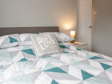 A bed with geometric patterned bedding a pillow with text on it and a bedside lamp at 17 Ffordd Gwenllian in Llanfairpwllgwyngyll