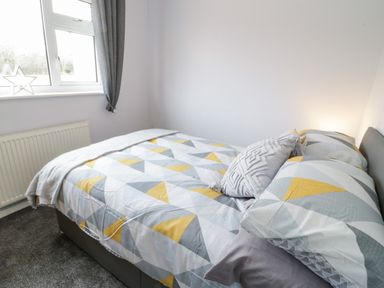 A bedroom with a bed covered in geometric patterned bedding next to a window at 17 Ffordd Gwenllian in Llanfairpwllgwyngyll