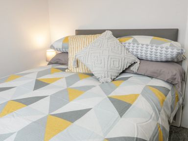 A bed with geometric patterned bedding and decorative pillows with a bedside lamp at 17 Ffordd Gwenllian in Llanfairpwllgwyngyll