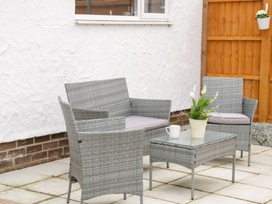 Outdoor patio with gray wicker chairs and glass top table with potted plant and cup at 17 Ffordd Gwenllian Llanfairpwllgwyngyll