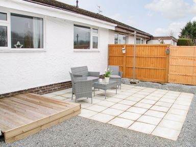 An outdoor patio with gray wicker furniture and a wooden fence at 17 Ffordd Gwenllian in Llanfairpwllgwyngyll