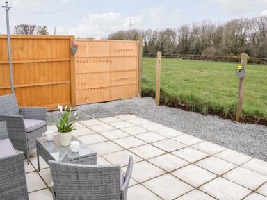 An outdoor patio with rattan chairs a glass table with a potted plant two mugs a wooden fence and green field at 17 Ffordd Gwenllian Llanfairpwllgwyngyll