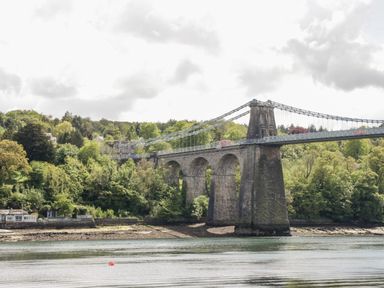A suspension bridge over a river with trees and buildings in the background at 17 Ffordd Gwenllian in Llanfairpwllgwyngyll