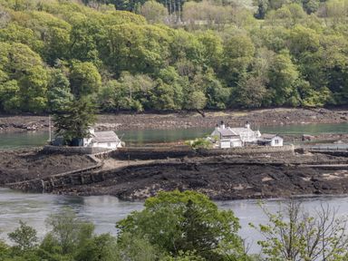 A small cluster of white buildings on rocky land by a river with trees in the background at 17 Ffordd Gwenllian in Llanfairpwllgwyngyll