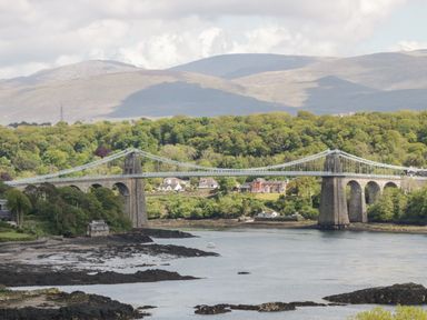 A suspension bridge over a river with houses and trees in the background at 17 Ffordd Gwenllian in Llanfairpwllgwyngyll