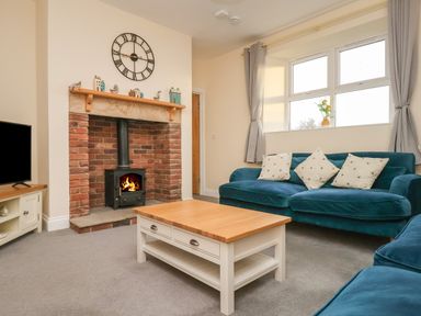 A living room with a fireplace a wooden coffee table and blue sofas at Garden Cottage in Alnmouth
