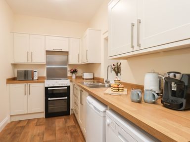 A kitchen with white cabinets wooden countertops a stove microwave and coffee machine at Garden Cottage in Alnmouth