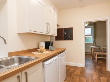 A kitchen with a wooden countertop sink cabinets appliances and a view into a dining room at Garden Cottage in Alnmouth