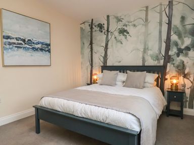 A bedroom with a bed with pillows and bedside tables with lamps and a forest mural on the wall at Garden Cottage in Alnmouth