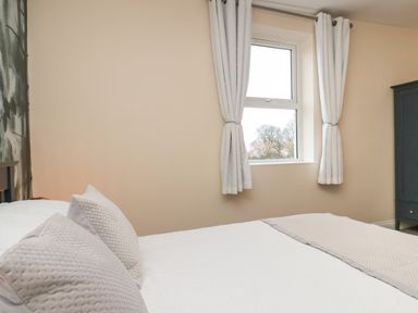 A bedroom with a bed with pillows and a window with curtains at Garden Cottage in Alnmouth