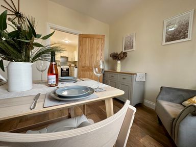 A dining room with a table set for two and a view into the kitchen at Garden Cottage in Alnmouth