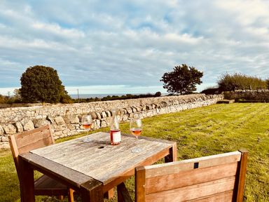 An outdoor area with a wooden table and two chairs a bottle and two glasses of rose on the table a stone wall and trees in the background at Garden Cottage in Alnmouth