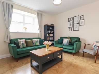A living room with two green sofas a wooden coffee table a gray armchair and a bookshelf at Pond Cottage in Alnmouth