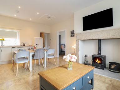 An open kitchen and dining area with a table set for four and a wood burning stove with TV above at Pond Cottage in Alnmouth
