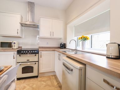 A kitchen with white cabinets stove microwave sink and kettle at Pond Cottage in Alnmouth