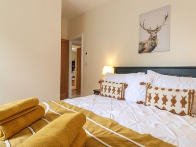 A bedroom with a made bed with white and brown pillows yellow towels and a painting of a deer at Pond Cottage in Alnmouth