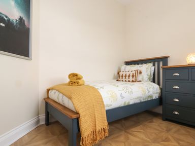 A bedroom with a single bed with floral bedding and yellow blankets next to a dark blue chest of drawers at Pond Cottage in Alnmouth