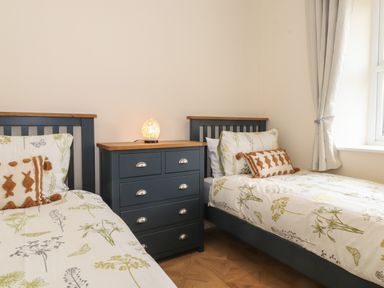 A bedroom with two single beds and a chest of drawers with a lamp between them at Pond Cottage in Alnmouth
