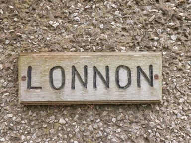 A wooden sign with the word LONNON mounted on a rough textured stone wall at Lonnon Cottage in Alnmouth